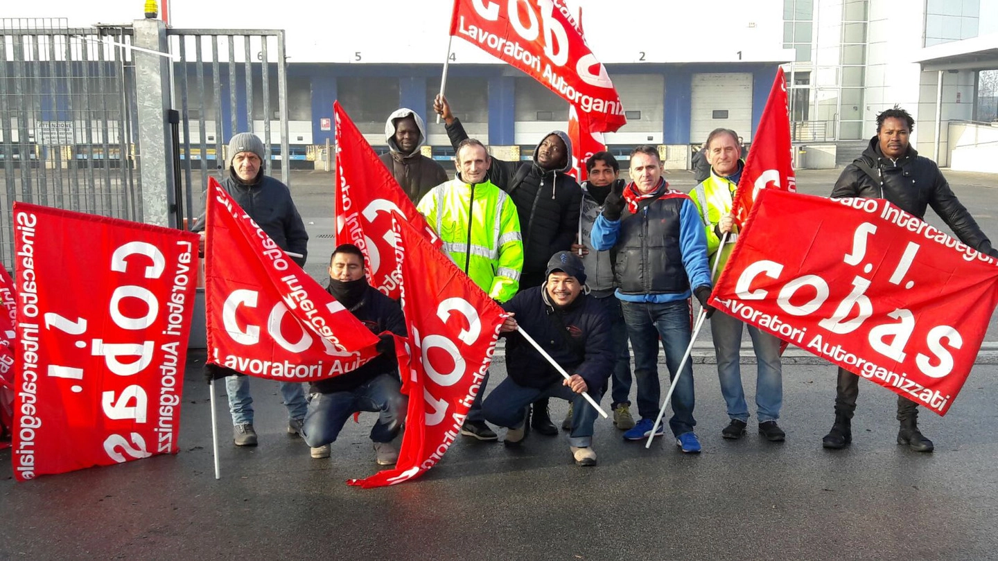 I lavoratori con le bandiere rosse dei Cobas davanti al cancello del polo logistico Transmec sulla Rivoltana