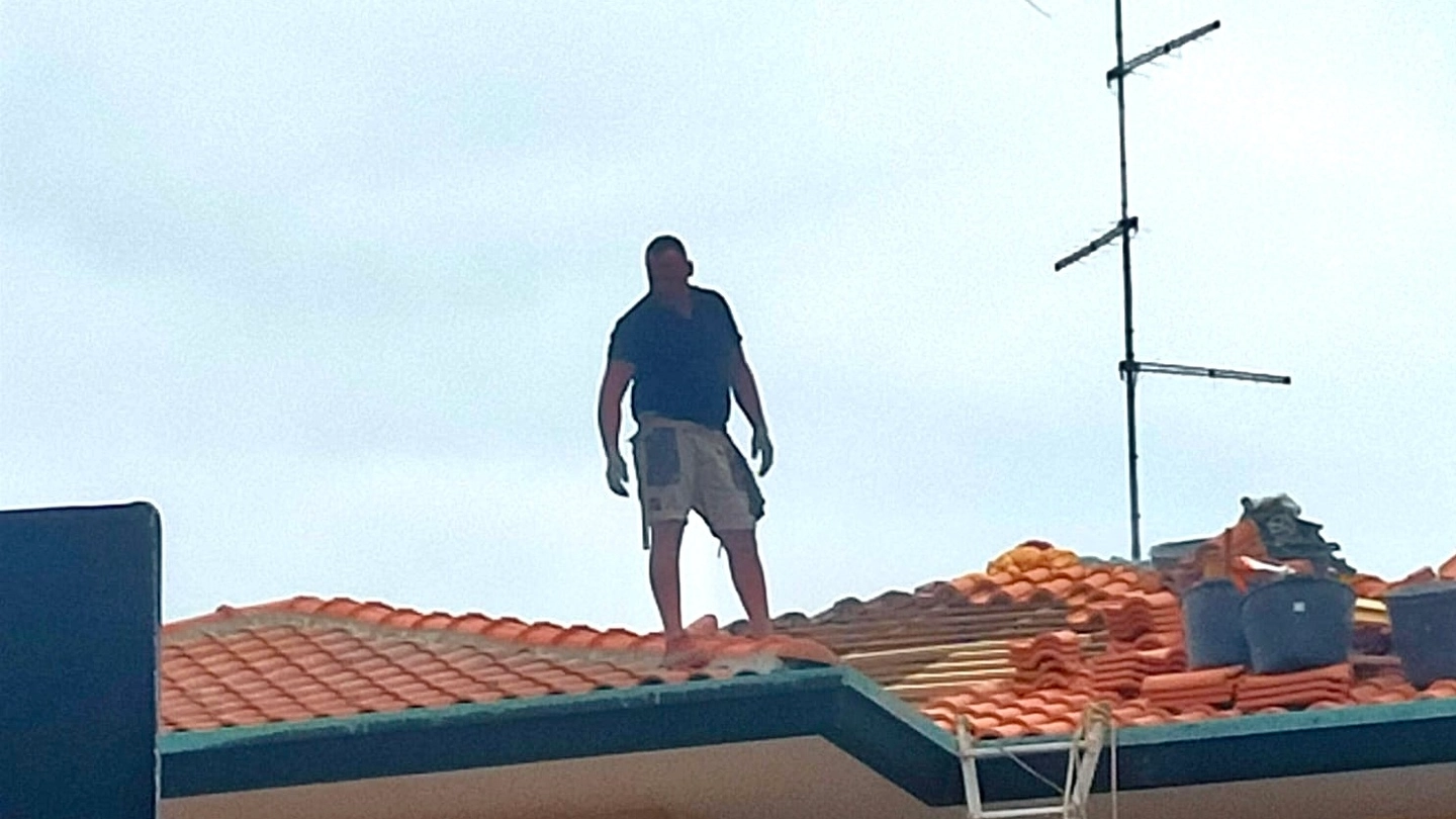 Un uomo sul tetto per riparare i danni della grandine