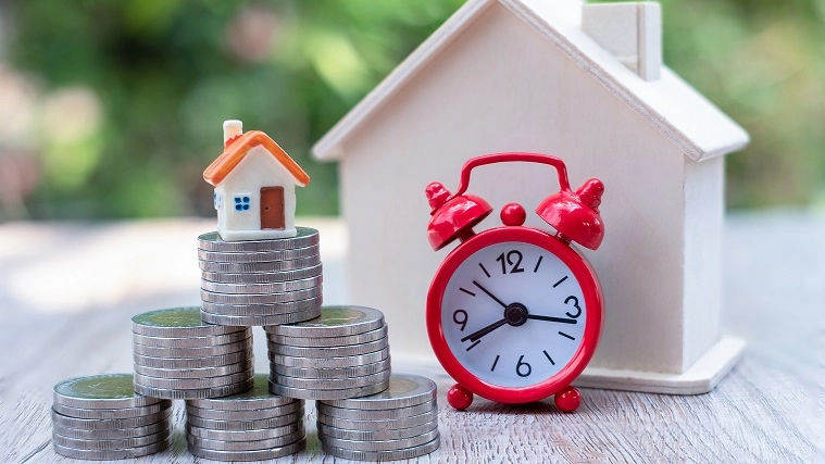 Coins, red alarm clock and home, time spent on financial concepts Real estate, mortgage, tax, rental, investment, finance, accounting and stock market.