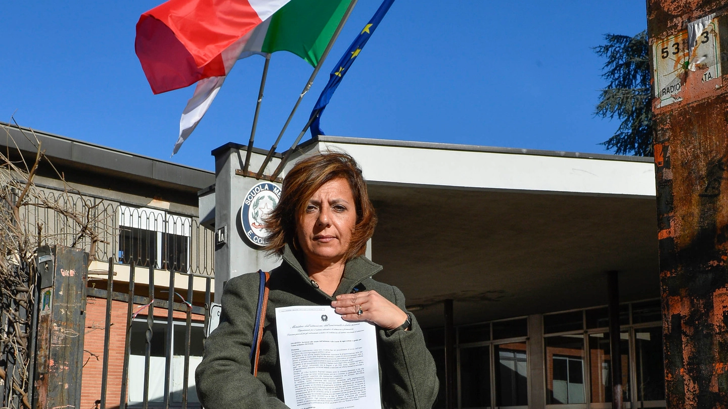 Caterina Scarselli davanti a scuola di Milano con in mano  il modulo  di iscrizione della figlia che a settembre andrà alle medie