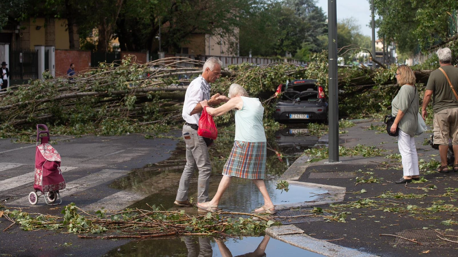 Un uomo aiuta un'anziana ad attraversare una via allagata
