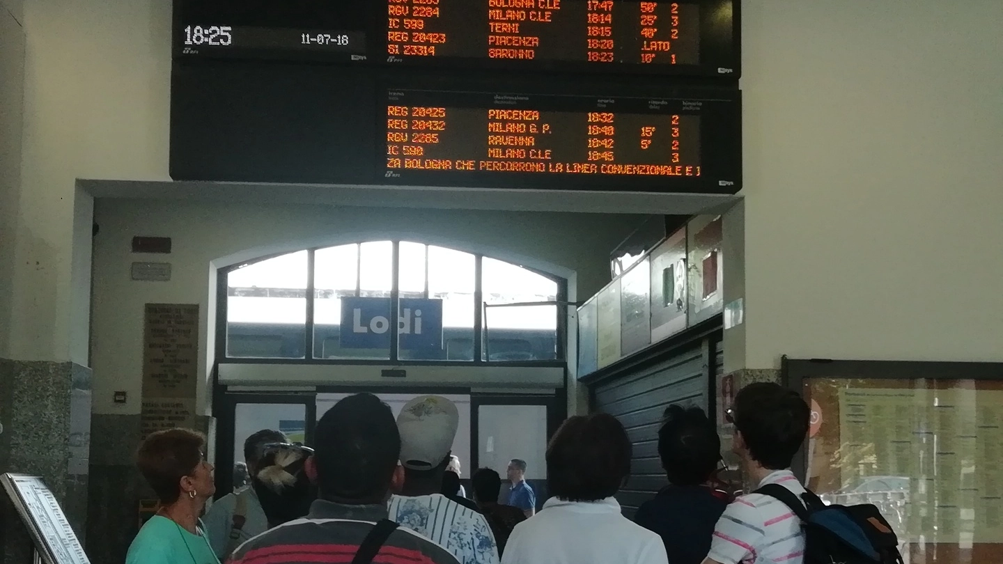 Viaggiatori in stazione a Lodi mentre controllavano il tabellone delle partenze con la comunicazione di ritardi e soppressioni