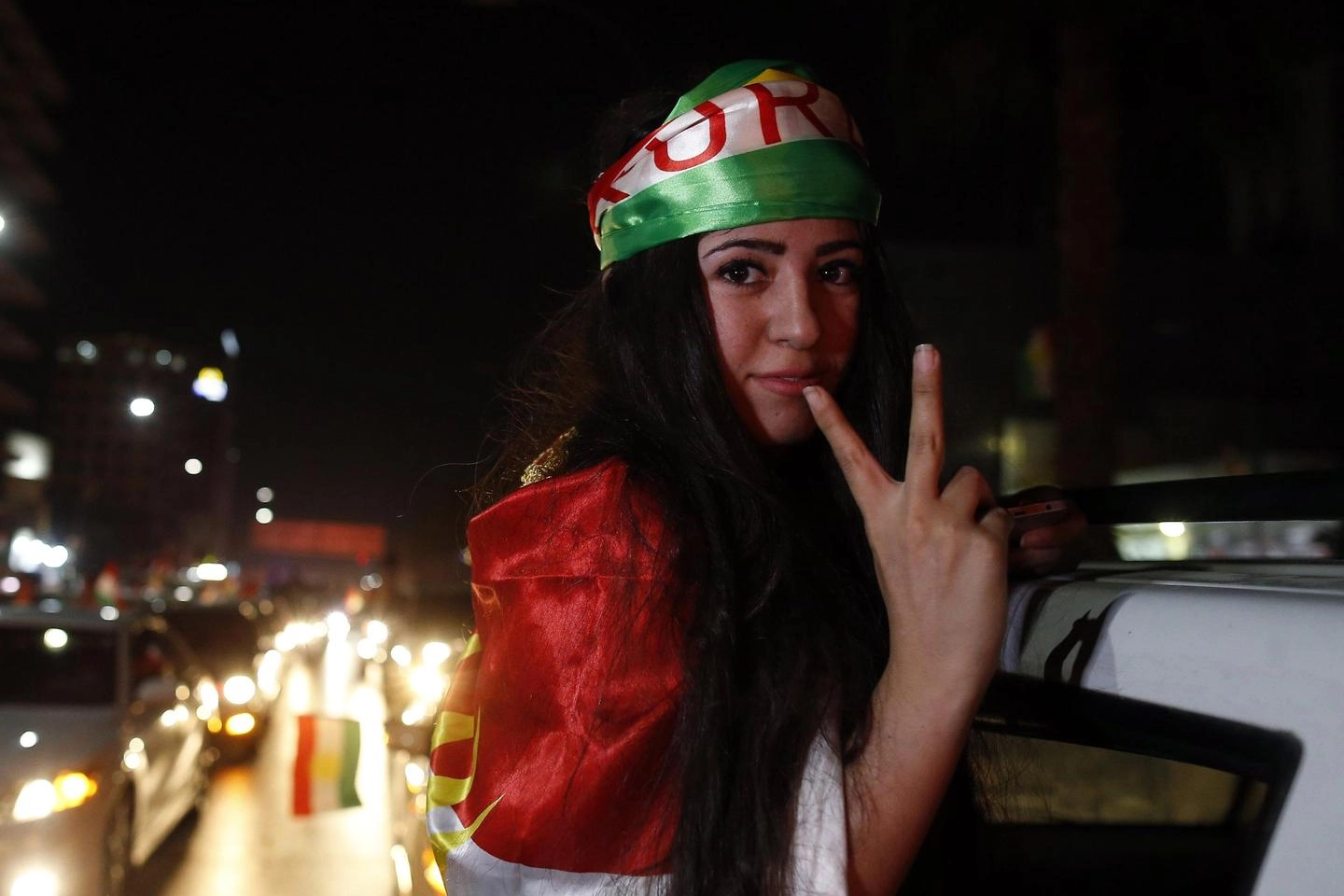 Una giovane curda festeggia in strada avvolta nei suoi colori