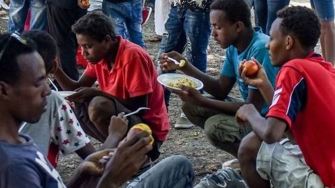 Un'immagine di repertorio di migranti intenti a consumare un pasto