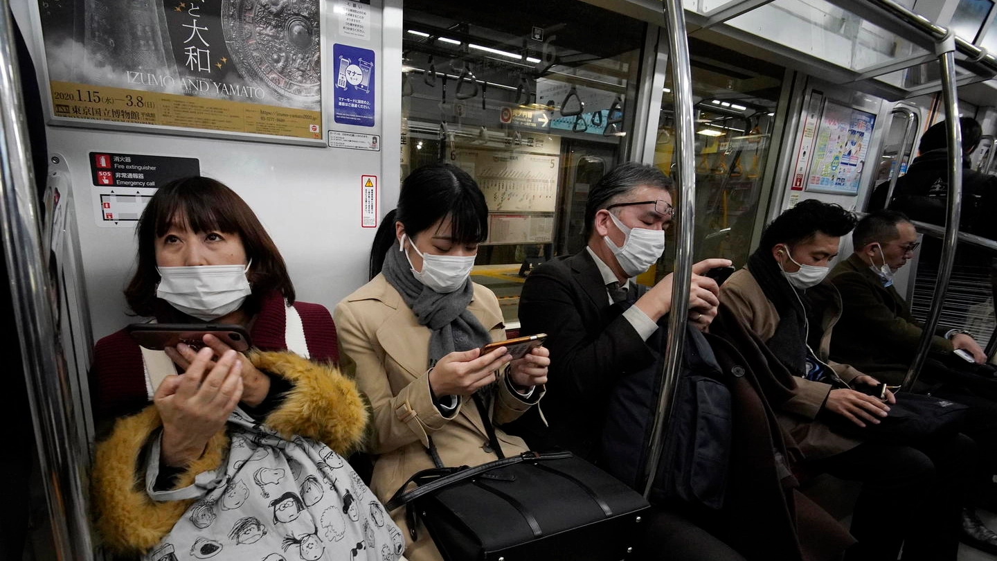 Persone con la mascherina nella metropolitana di Tokyo (Ansa)