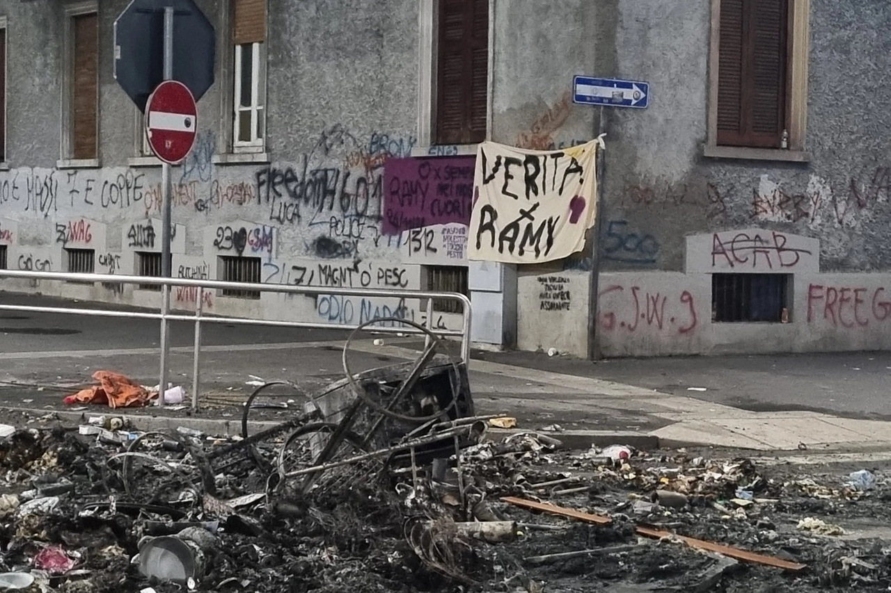 I resti dell'incendio notturno al Corvetto appiccati dagli amici di Ramy Elgaml e lo striscione appeso