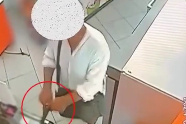 Il rapinatore mentre estrae la pistola nel negozio di surgelati