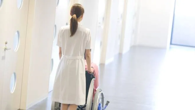 BJTYCF Nurse pushing patient in wheelchair along a corridor infermiera