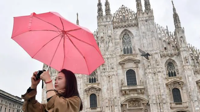 Una turista asiatica fotografa piazza Duomo proteggendosi dalla pioggia con un ombrello, Milano, 2 maggio 2018. Un'area di bassa pressione è la causa di una fase di maltempo che dovrebbe durare sulle regioni settentrionali per una decina di giorni. ANSA/DANIEL DAL ZENNARO
