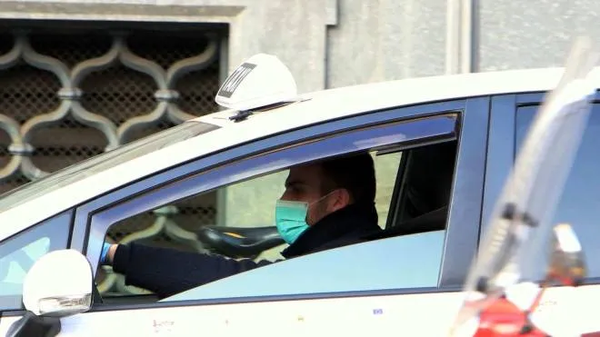 Coronavirus, un tassista con il suo taxi, indossa guanti e mascherina, Milano 24 febbraio 2020, ANSA / PAOLO SALMOIRAGO