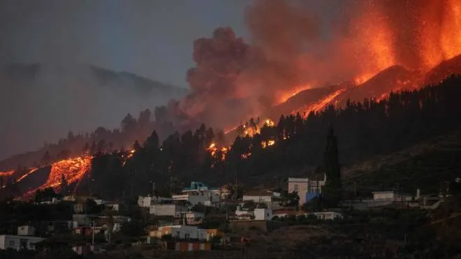 A river of lava approaches houses as Mount Cumbre Vieja erupts in El Paso, spewing out columns of smoke, ash and lava as seen from Los Llanos de Aridane on the Canary island of La Palma on September 19, 2021. - The Cumbre Vieja volcano erupted on Spain's Canary Islands today spewing out lava, ash and a huge column of smoke after days of increased seismic activity, sparking evacuations of people living nearby, authorities said. Cumbre Vieja straddles a ridge in the south of La Palma island and has erupted twice in the 20th century, first in 1949 then again in 1971. (Photo by DESIREE MARTIN / AFP)