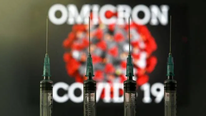 An illustration picture taken in London on December 2, 2021 shows four syringes and a screen displaying the word 'Omicron',  the name of the new covid 19 variant, and an illustration of the virus. (Photo by Justin TALLIS / AFP)
