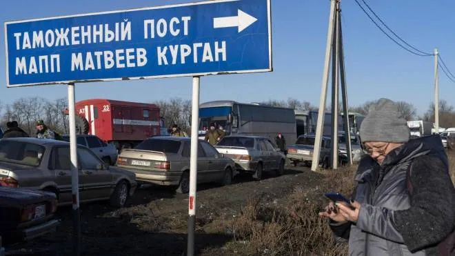 A woman looks at her mobile phone near a queue of cars as they cross the Russian border check point near the town of Uspenka, on February 19, 2022. - A Russian region bording Ukraine declared a state of emergency on February 19, 2022, citing growing numbers of people arriving from separatist-held regions in Ukraine after they received evacuation orders. (Photo by Andrey BORODULIN / AFP)