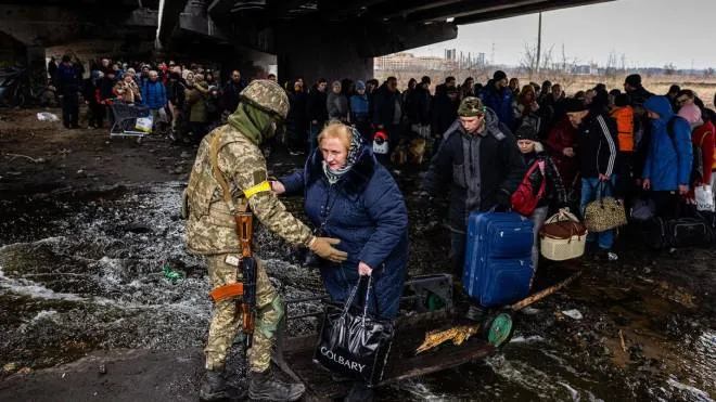 TOPSHOT - A Ukrainian serviceman helps evacuees gathered under a destroyed bridge, as they flee the city of Irpin, northwest of Kyiv, on March 7, 2022. - Ukraine dismissed Moscow's offer to set up humanitarian corridors from several bombarded cities on March 7, 2022, after it emerged some routes would lead refugees into Russia or Belarus. The Russian proposal of safe passage from Kharkiv, Kyiv, Mariupol and Sumy had come after terrified Ukrainian civilians came under fire in previous ceasefire attempts. (Photo by Dimitar DILKOFF / AFP)