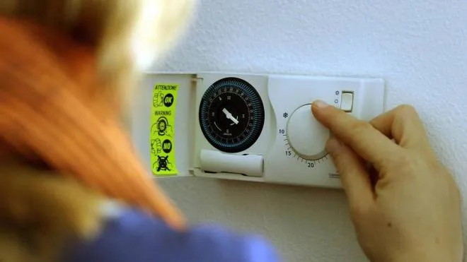 Una donna regola il termostato di un impianto di riscaldamento a gas in una foto d'archivio. ANSA/FOLCO LANCIA