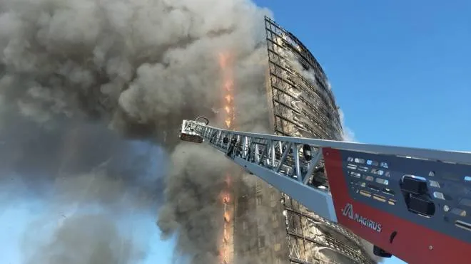 La torre di via Antonini mentre brucia, vigili del fuoco durante l’intervento sullo scheletro del grattacielo dopo il rogo e auto carbonizzate dopo che le fiamme hanno avvolto interamente l’edificio