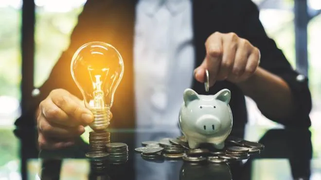 A businesswoman putting coin into piggy bank and a light bulb over coins stack on the table for saving money and financial concept